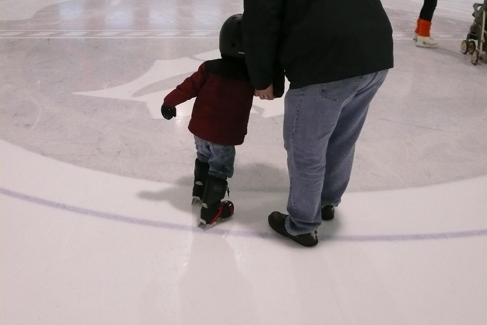 A small child holding an adult's hand on rink ice