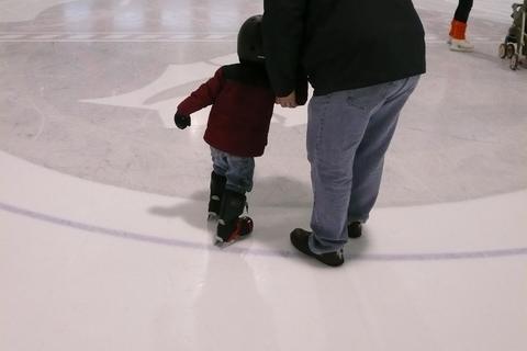 A small child holding an adult's hand on rink ice