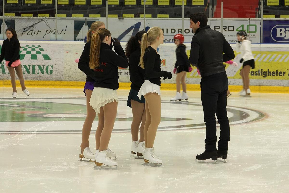 Young figure skaters listening to a coach at the boards