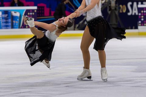 Synchronized skaters pulling a teammate into a low spiral
