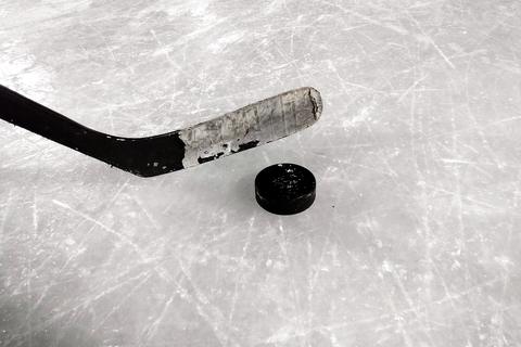 A taped hockey stick blade beside a puck on scratched ice