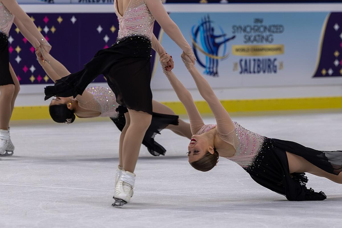 Synchronized skaters in a linked spiral, one leaning back almost to the ice